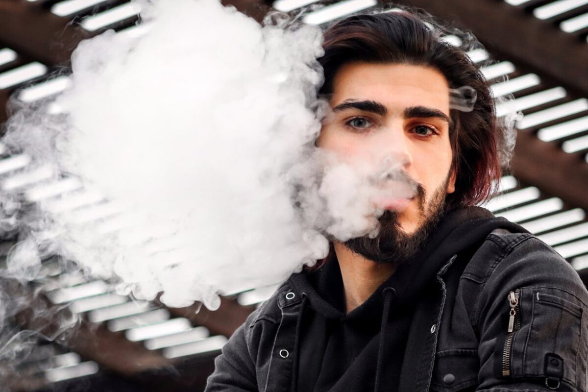 about-02 Man with a beard vaping outdoors, releasing smoke clouds in Dubai.