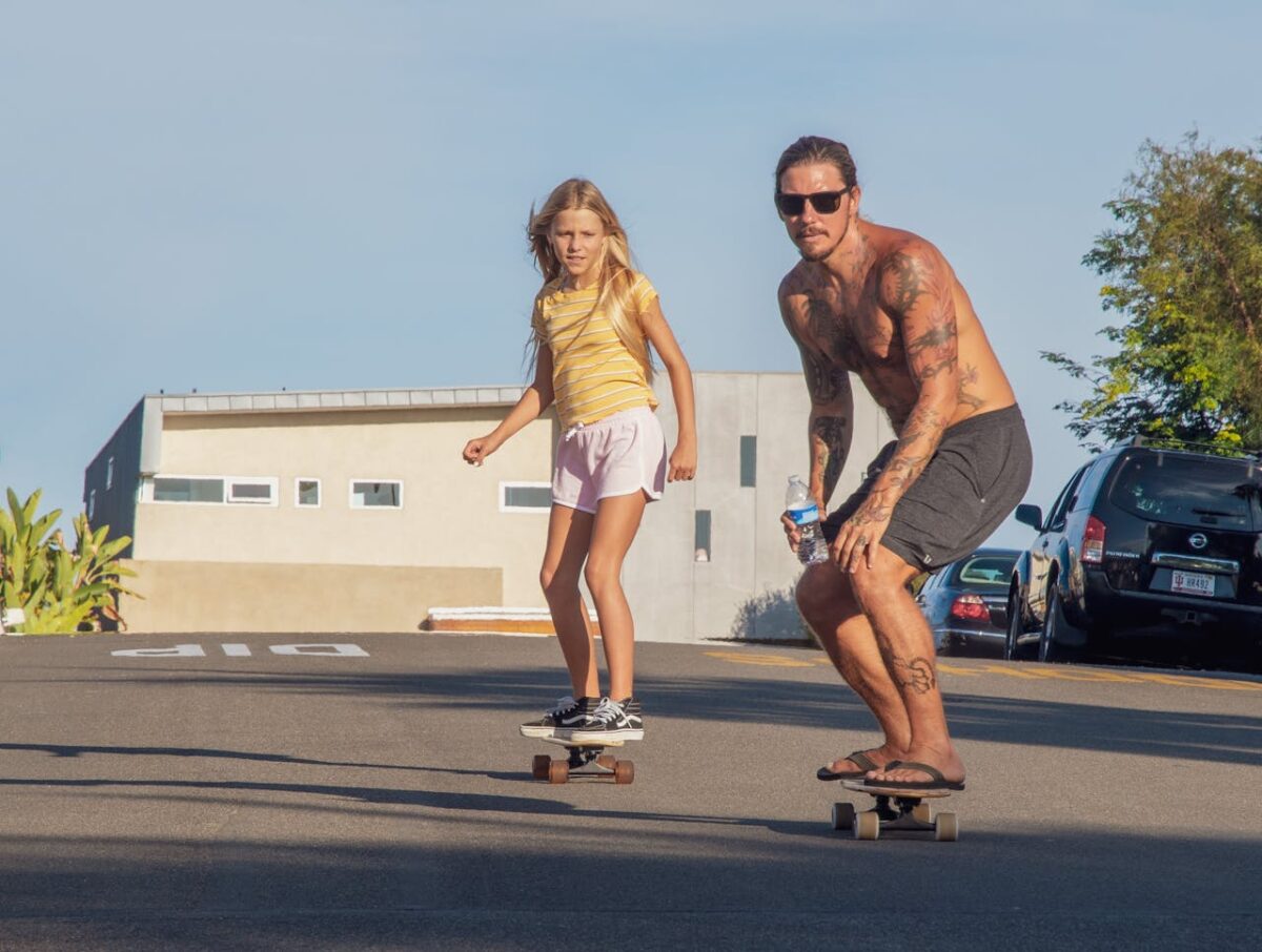 Father and daughter enjoying a sunny skateboarding session on a suburban street.