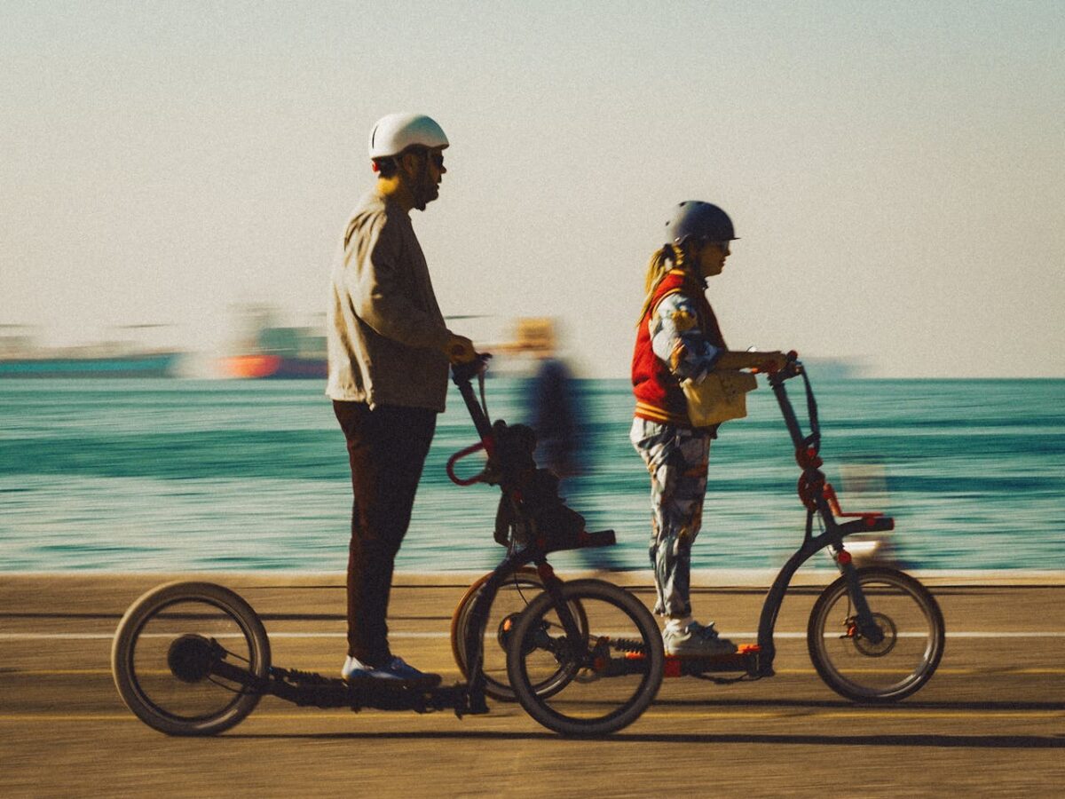 A man and woman enjoying a sunny day riding electric scooters along the seaside promenade.